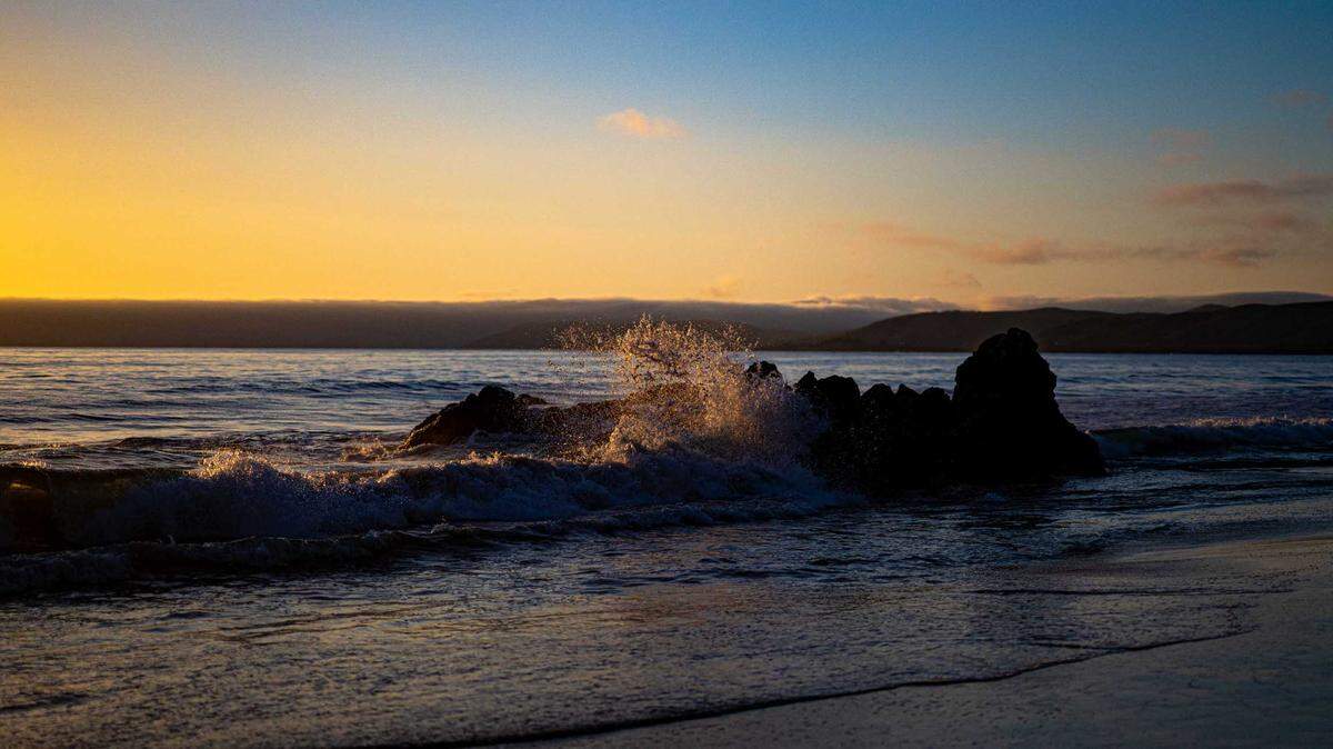 Longer-period waves break on the rocks on Atascadero Beach with the marine layer in the background.