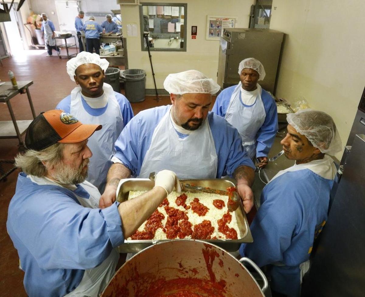 James Daniel ladles marinara sauce while Pedro Anaya holds a lasagna pan as inmates in the California Men’s Colony’s culinary arts program prepare a meal in 2017.