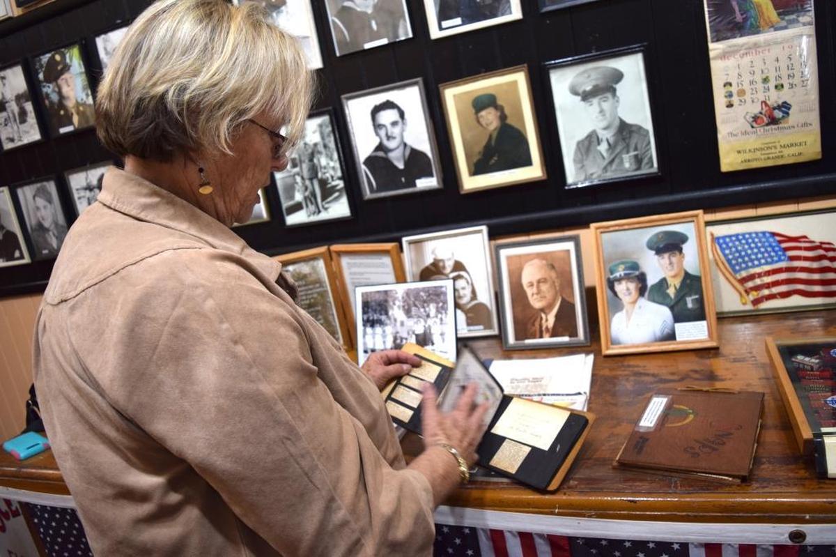 Linda Austin, curator of the Oceano Depot, looks through a scrapbook of newspaper clippings kept by Pfc. George Murray’s mother, regarding local involvement in World War II. Around her are photos of the local men and women that served in World War II, including Murray on the far right.