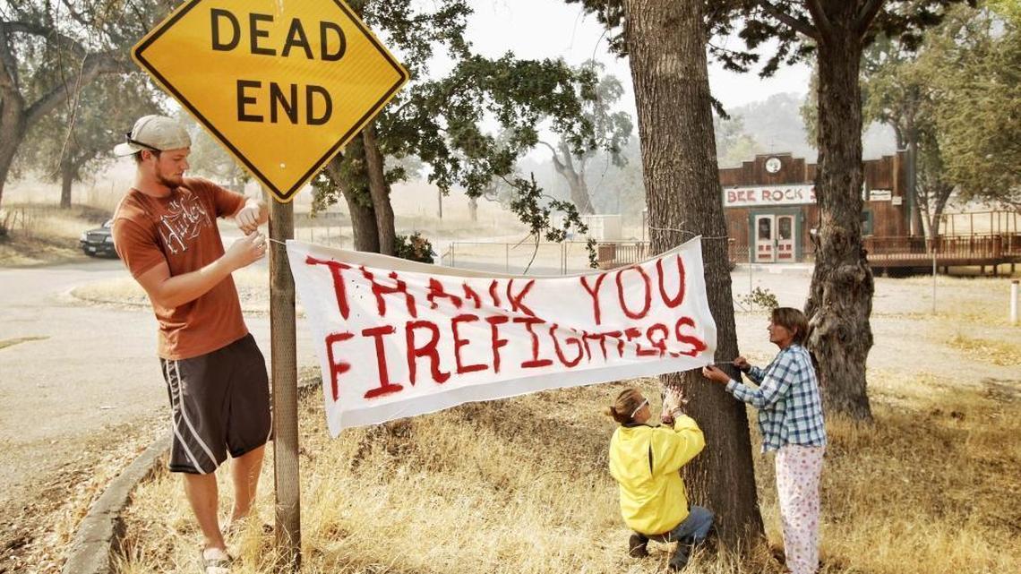 Nate Broden, left, Mallory Doiel-Glisson, and Dawn Leigh Doiel hang up a sign thanking firefighters at the intersection of Interlake and Bee Rock roads. They are opting to stay at their home despite a mandatory evacuation order.