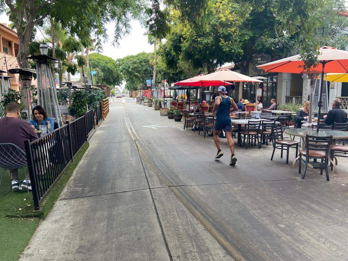 A man runs down State Street in Santa Barbara while diners eat in outdoor parklets. In spring 2020, the city closed the street to car traffic to boost business. The City Council has supported making the change permanent.