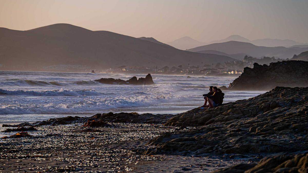 People look out over the ocean in Cayucos as by-the-wind sailors wash up on the beach.