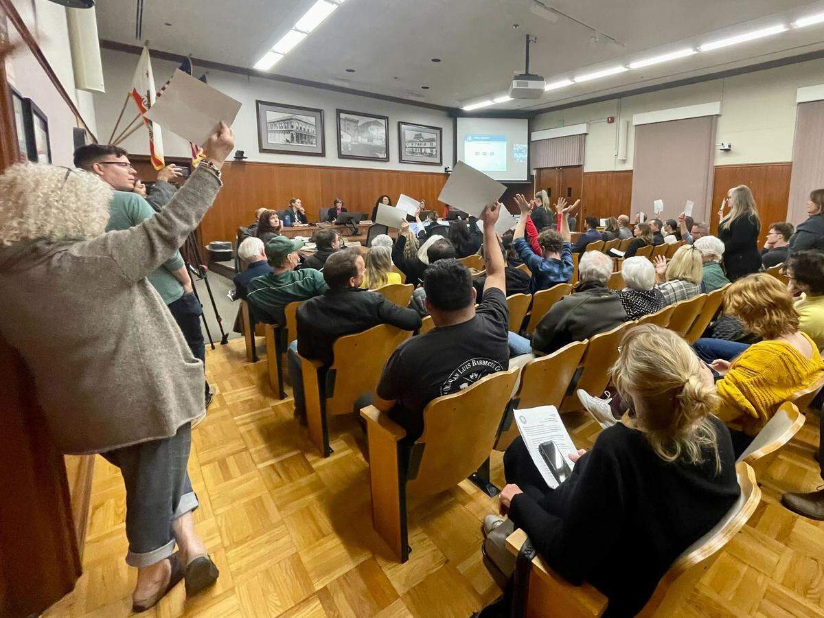 Attendees hold up signs at the San Luis Obispo City Council on Nov. 7, 2023, as speakers share how parking challenges were impacting the downtown.