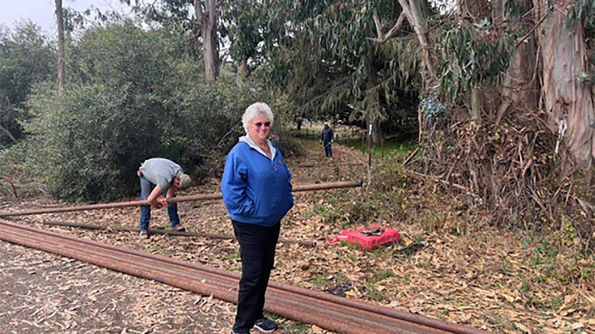 Morro Bay Audubon President Judy Neuhauser stands in front of new 3rd street entrance to the Sweet Springs Nature Preserve in Los Osos as workers from SmithCo Construction install improvements.