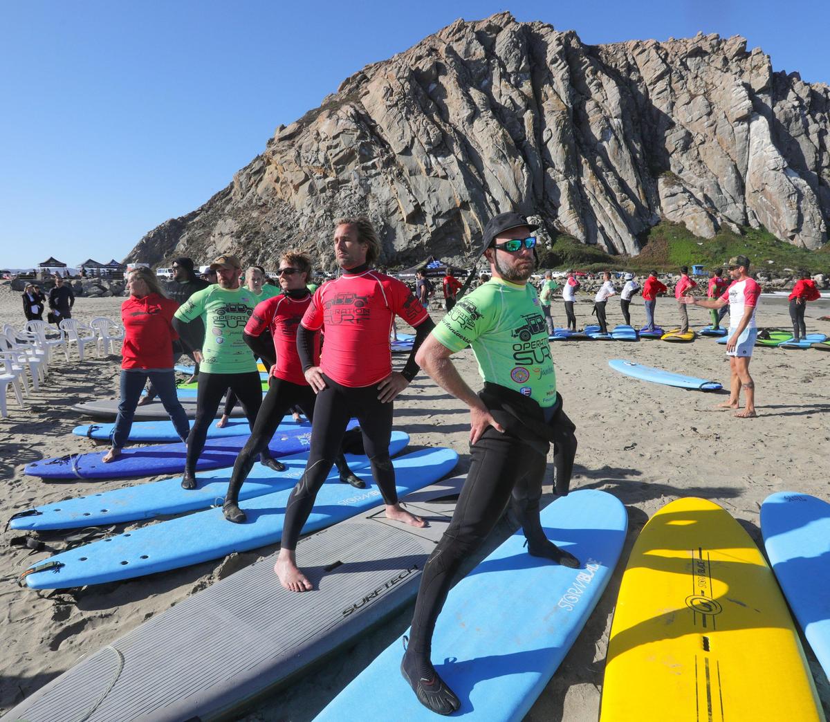 Dominic Green, center of the circle, leads a group in yoga in Morro Bay on Wednesday before heading out on the water as part of Operation Surf’s week of teaching veterans to surf.
