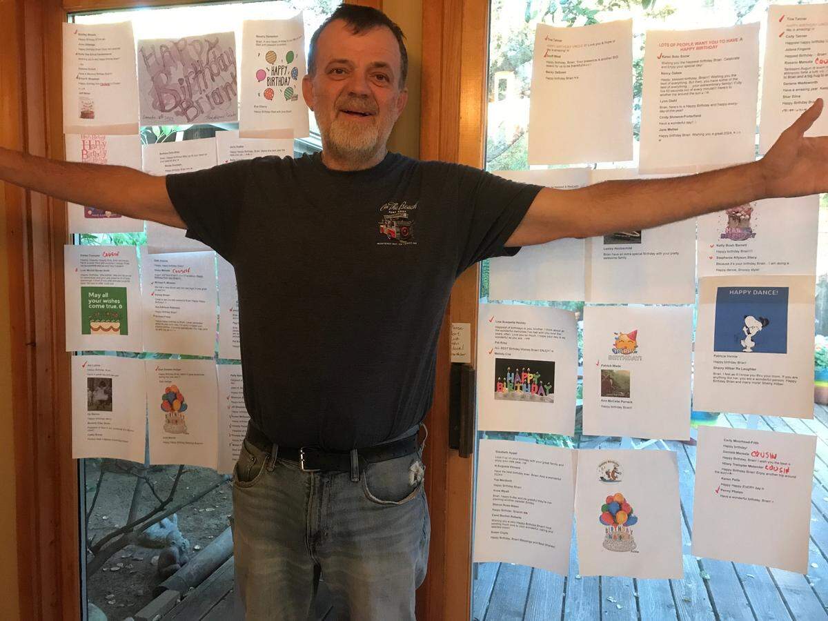 Brian Tanner stands in front of a collection of birthday greetings that his mother, Kathe Tanner, printed out and taped to the glass doors a few years ago. He died suddenly June 11, 2025.