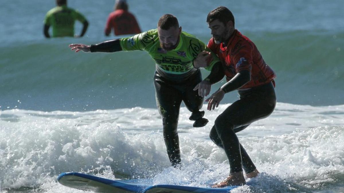 An Operation Surf instructor, right, helps a veteran stand up on a surfboard during a 2016 event in Avila Beach.