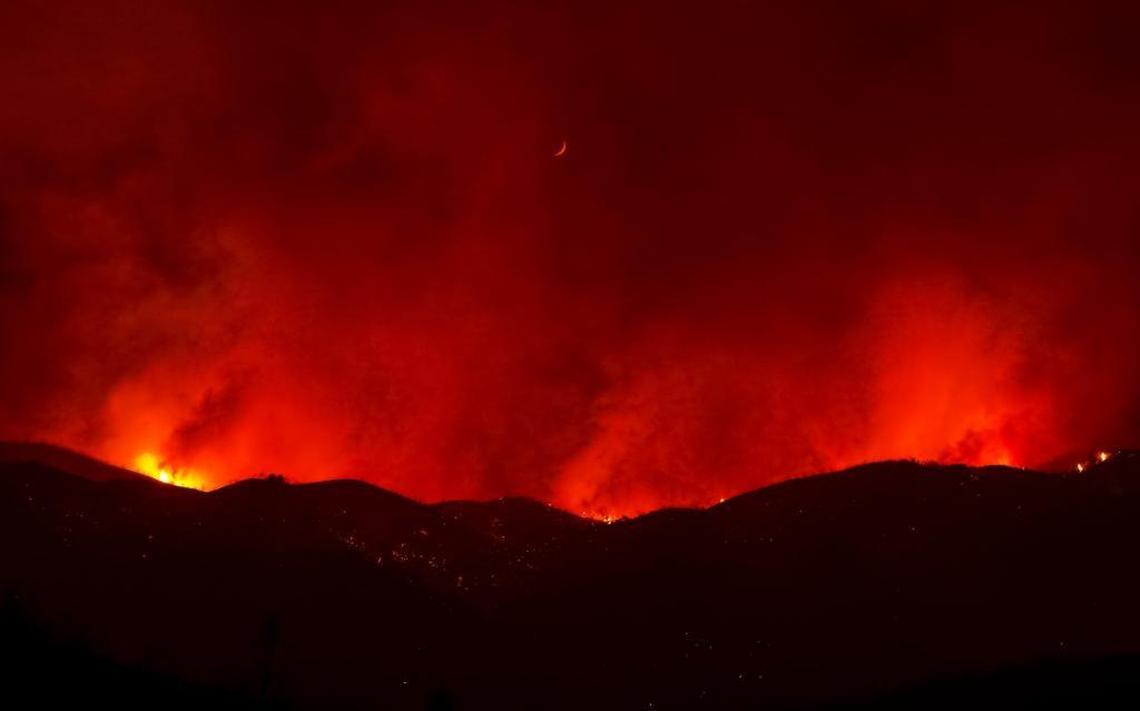 A crescent moon hovers over the red glow of the Hill Fire seen here near Huer Huero Road.