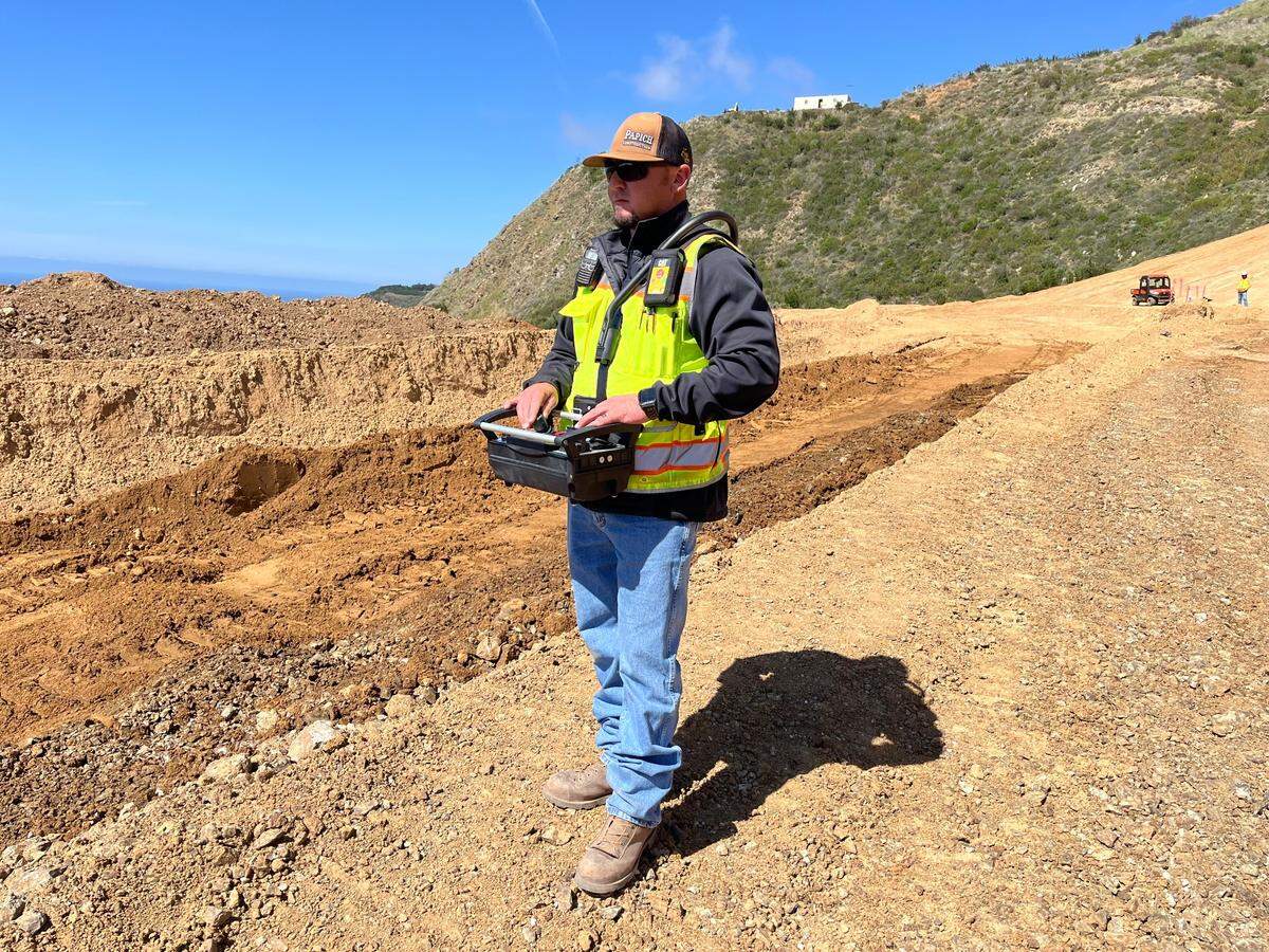 A heavy equipment operator uses a remote control to maneuver an excavator while working at the site of the Regent’s Slide on Highway 1. The innovative technology can both improve productivity and enhance work safety on potentially dangerous slopes.