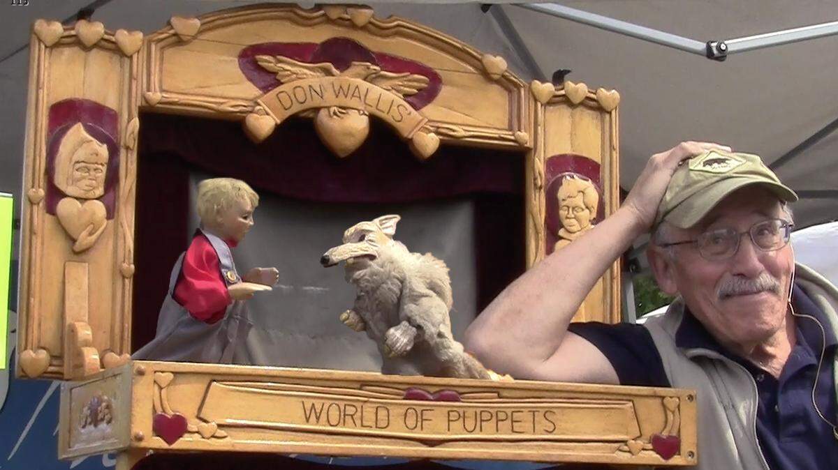 Don Wallis leans on his mobile stage with a couple of his handmade puppets.