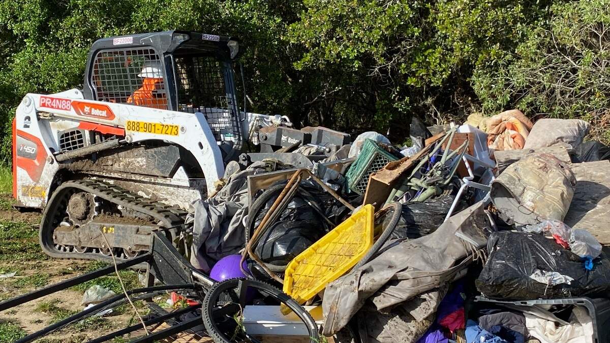 A hazmat-suited Caltrans worker scrapes up some of the approximately 80 cubic yards of debris and miscellaneous belongings from a large encampment alongside Highway 1 in Cambria. The cleanup was done Monday, April 18.