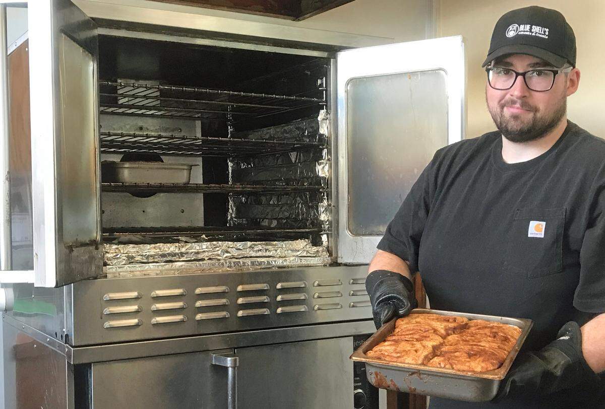 Nick Fleischmann, co-owner of Blue Shell’s Sweets & Treats in Morro Bay, shifts some of the shop’s cinnamon rolls to the top shelf of the oven to finish the baking and browning process. When the rolls are upended out of the baking pan, the sticky “cinnamon goo” topping takes center stage.