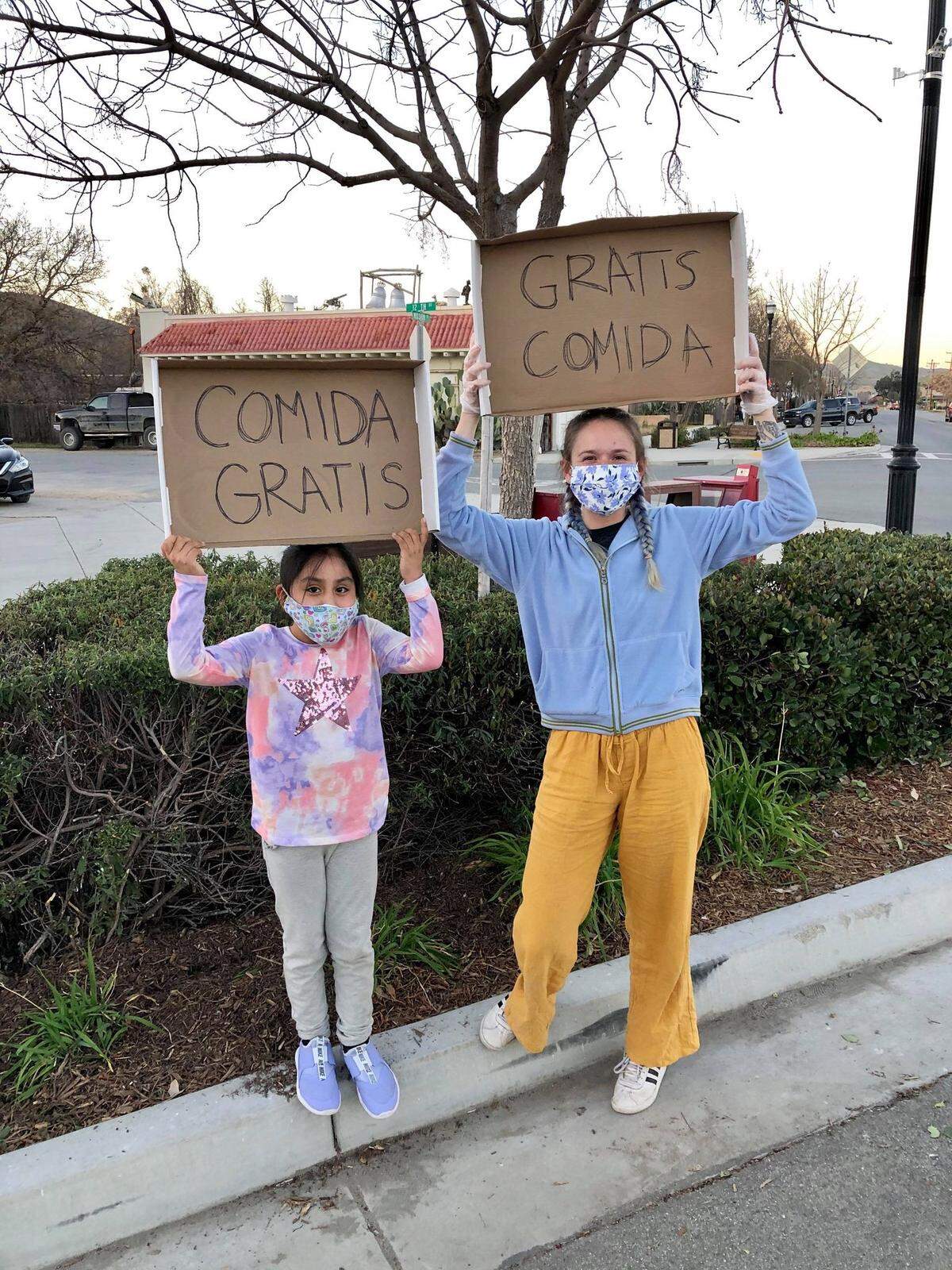 Volunteers hold signs that say “free food” in Spanish during a distribution event organized by Mujeres de Acción, a North County community organization. The group has been helping Spanish-speaking families during the coronavirus pandemic by giving out food and supplies and sharing information on a Spanish-language COVID-19 Facebook page.