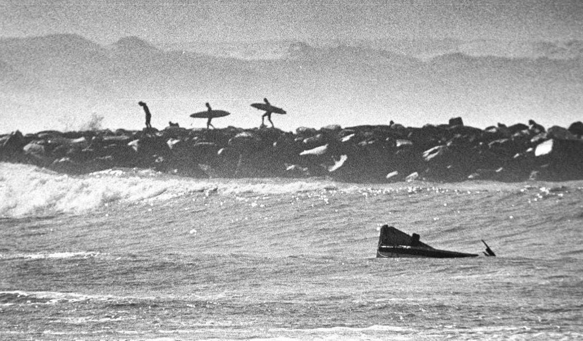 Surfers watch from Morro Bay breakwater as the broken prow of the San Mateo bobs in the ocean after the boat capsized on Feb. 16, 1983.