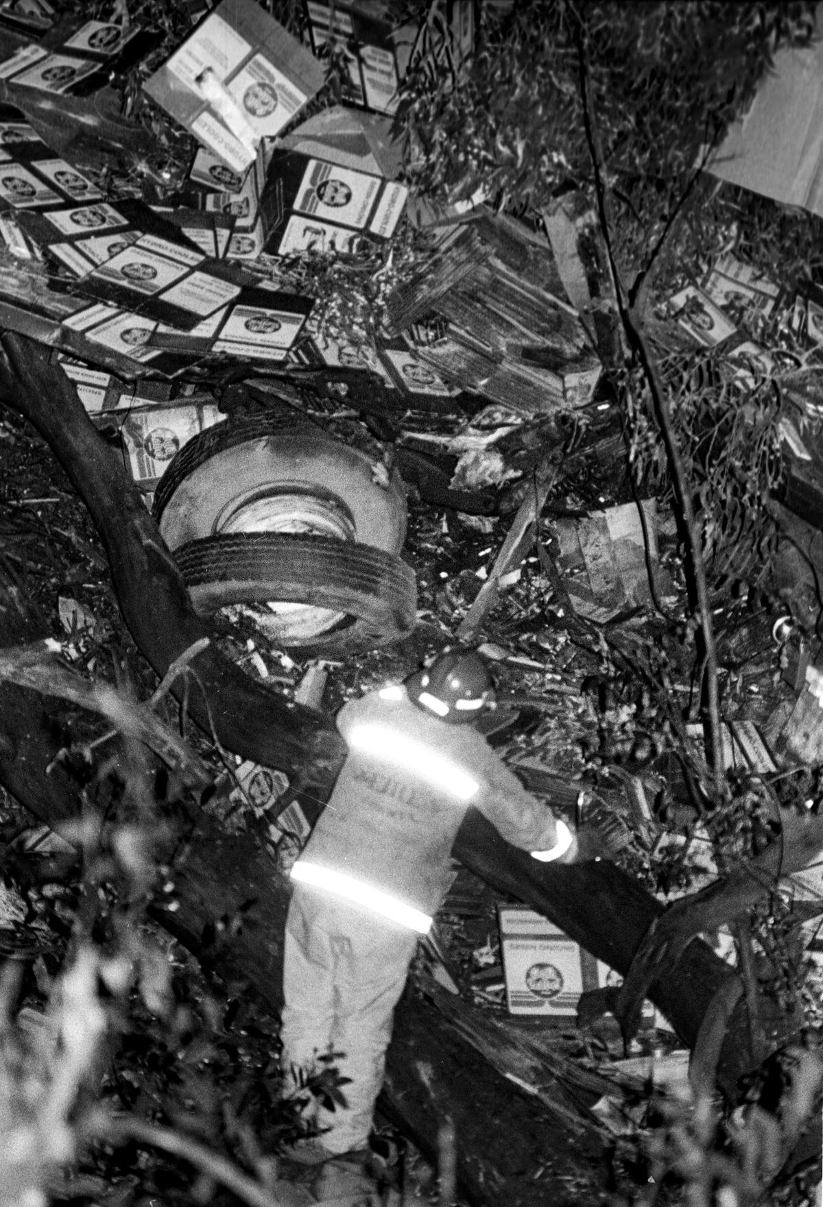 Firefighter surveys the scene of a fatal semi-trailer truck crash on the Cuesta Grade near San Luis Obispo in 1984. The wheels of the truck lie amid cardboard boxes.