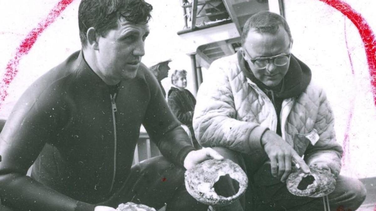 This 1963 photo is from a print showing editing marks. Fish and Game biologists Dick Poole, left and Keith Cox hold up evidence of abalone killed by sea otters that have migrated into north county coastal waters. Some shells were freshly broken.