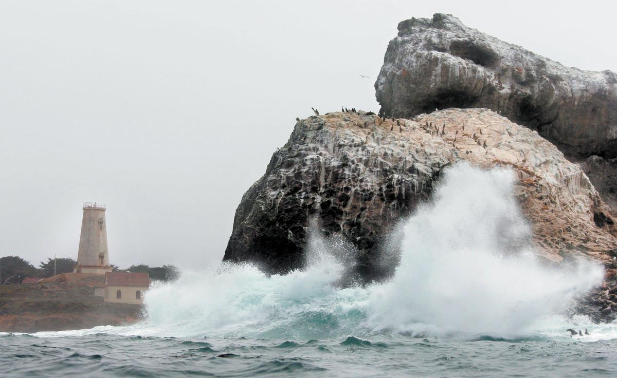 A wave crashes against the rocks in front of the Piedras Blancas Light Station north of San Simeon. The pale-colored stones gave Piedras Blancas its name.