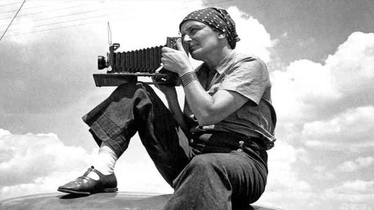 Dorothea Lange sits on her care while shooting with her Graflex camera.