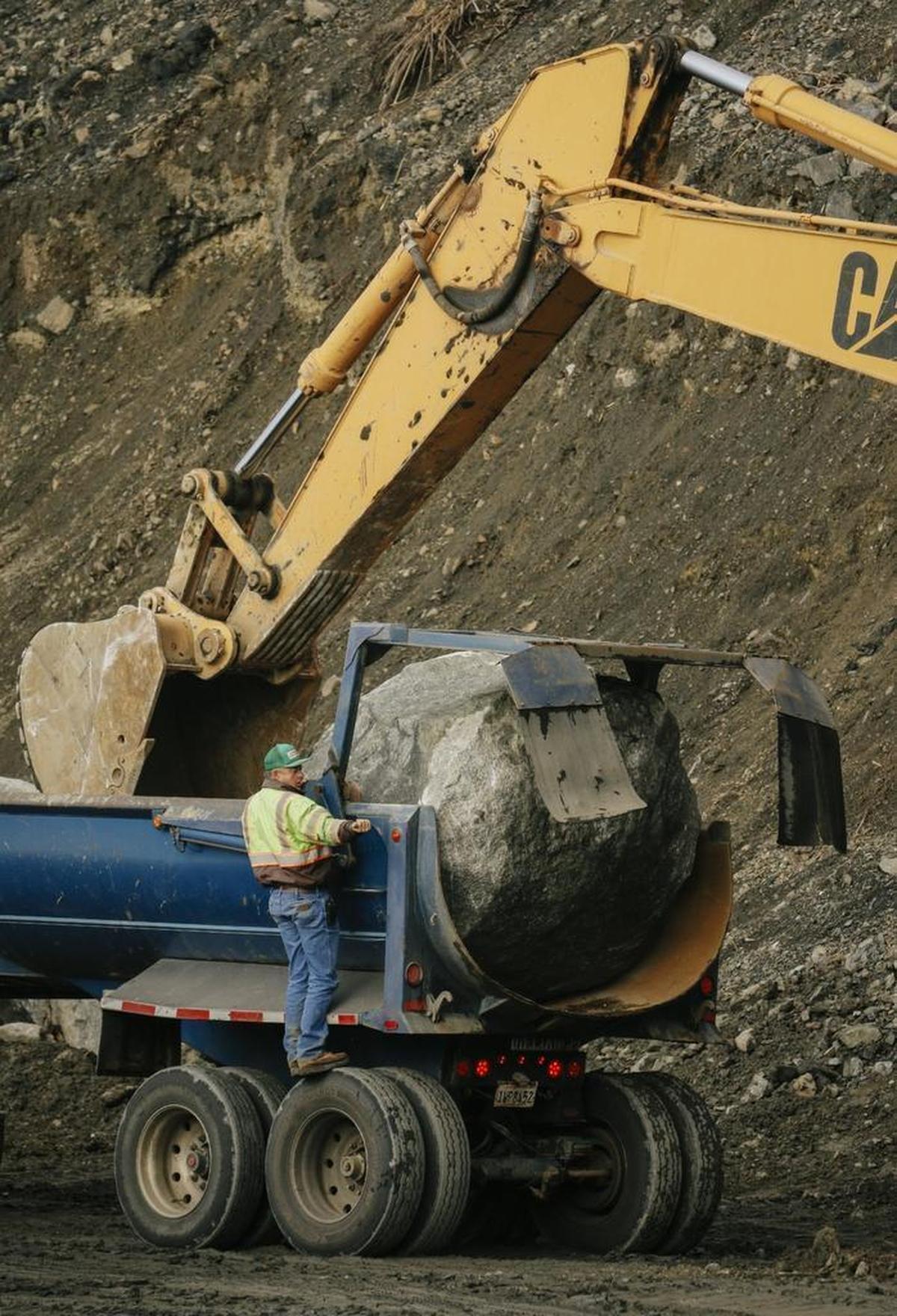 A worker guides an excavator to remove a newly arrived boulder from a truck on Thursday as crews continue to work to build a road over the Mud Creek Slide on Highway 1 along the Big Sur coast.