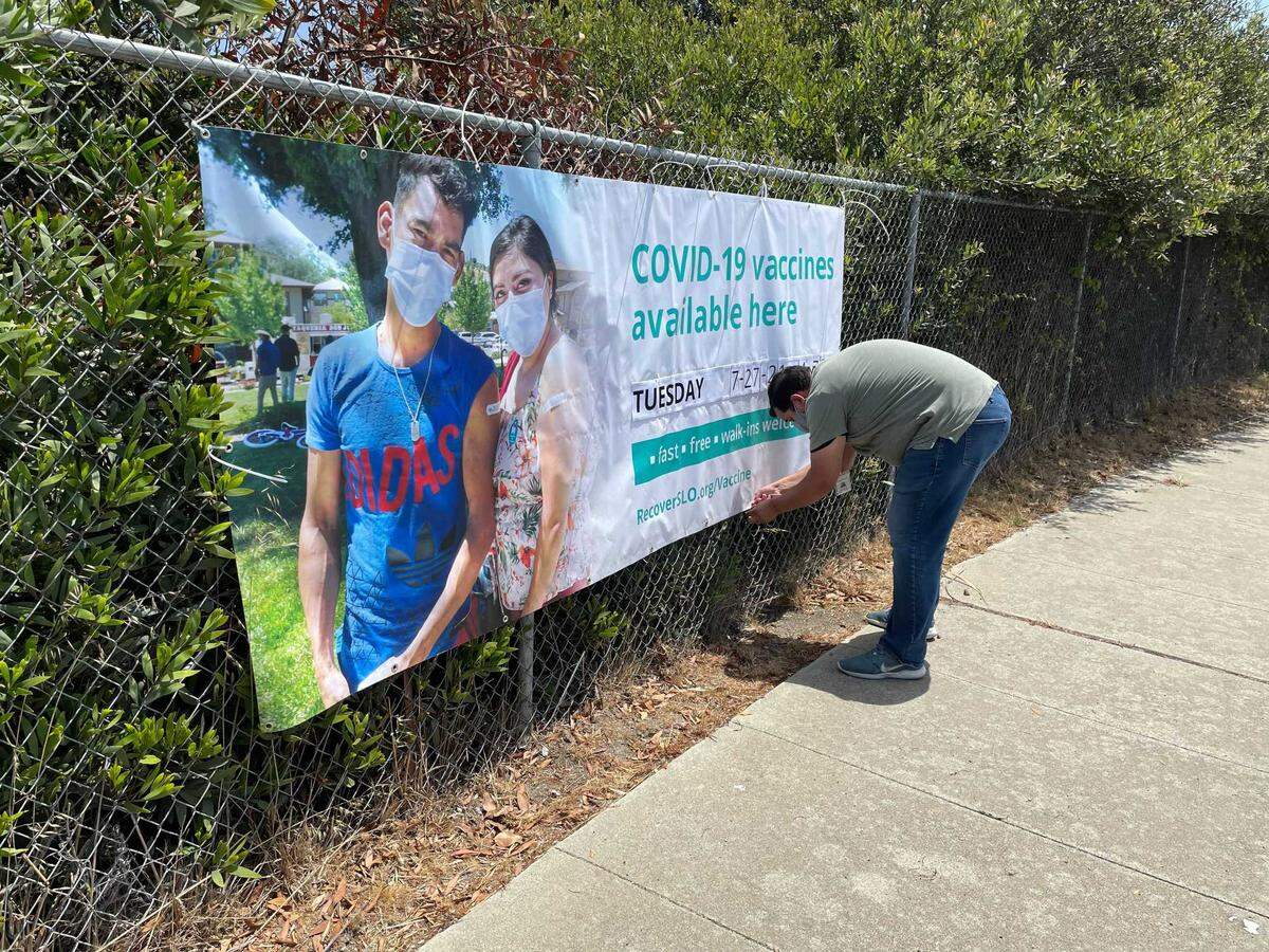 Felipe Gonzalez hangs a banner advertising a San Luis Obispo County Public Health Department coronavirus vaccine clinic in San Simeon. Gonzalez is the agency’s multilingual outreach coordinator, which involves canvassing in communities with lower vaccination rates and distributing information about nearby shot clinics.