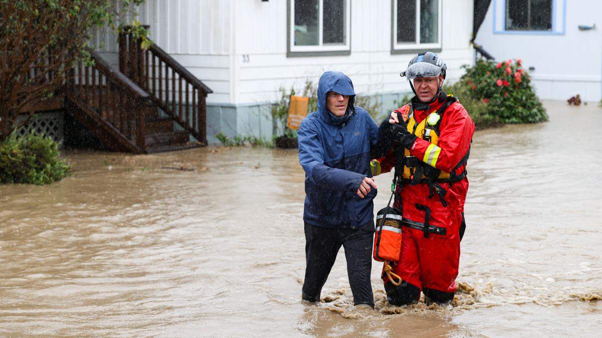 Jeff Spencer, resident at Oak Terrace Mobile Home Park in Cambria is assisted through knee deep water by Capt. Michael Burkey with Cambria Fire as Santa Rosa Creek flooded and triggering evacuations on March 10, 2023.