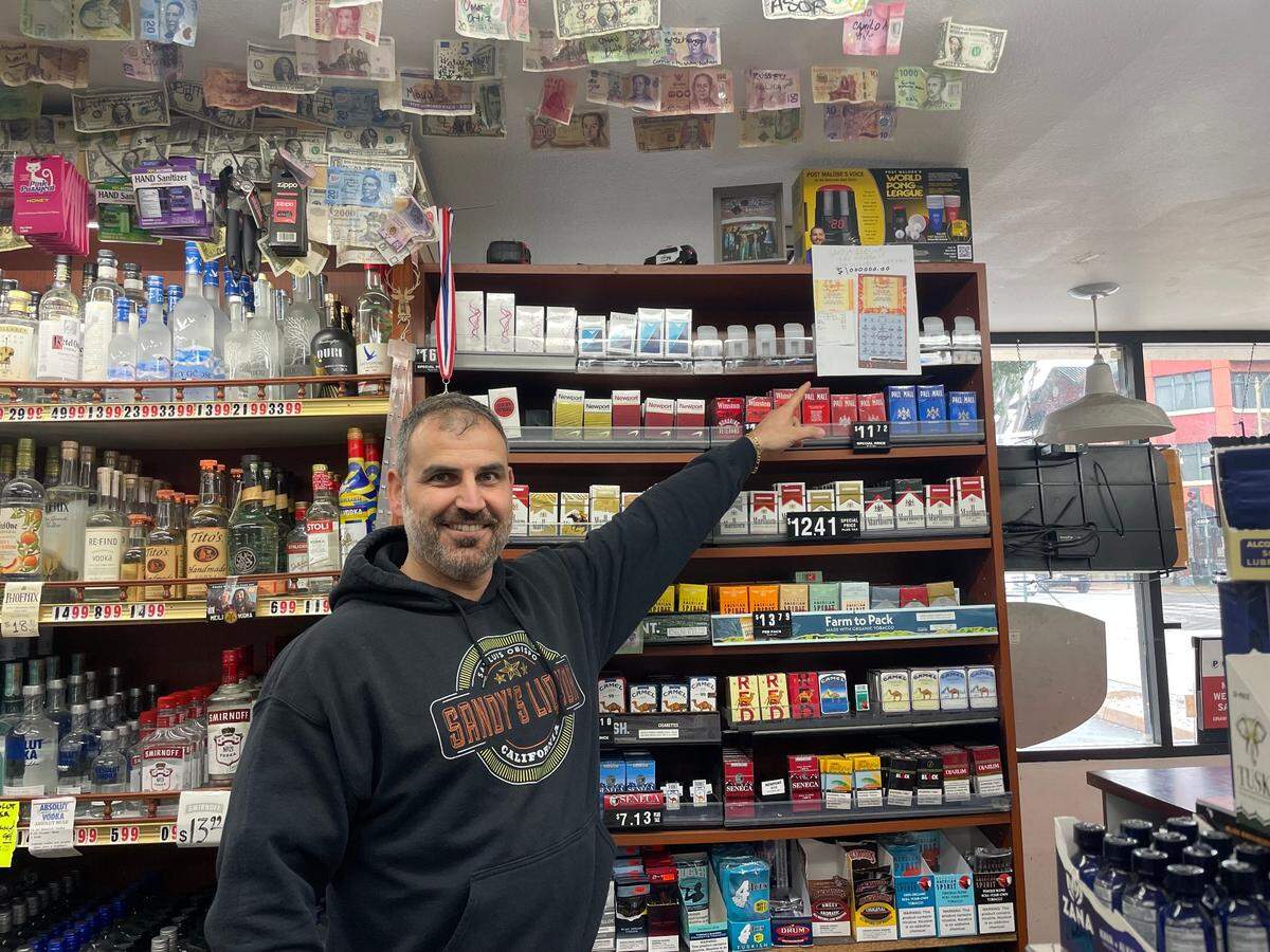 Sandy’s Deli-Liquor store manager Wilson Samaan points to the $1 million winning scratcher that a customer bought at the store on April 6, 2025.