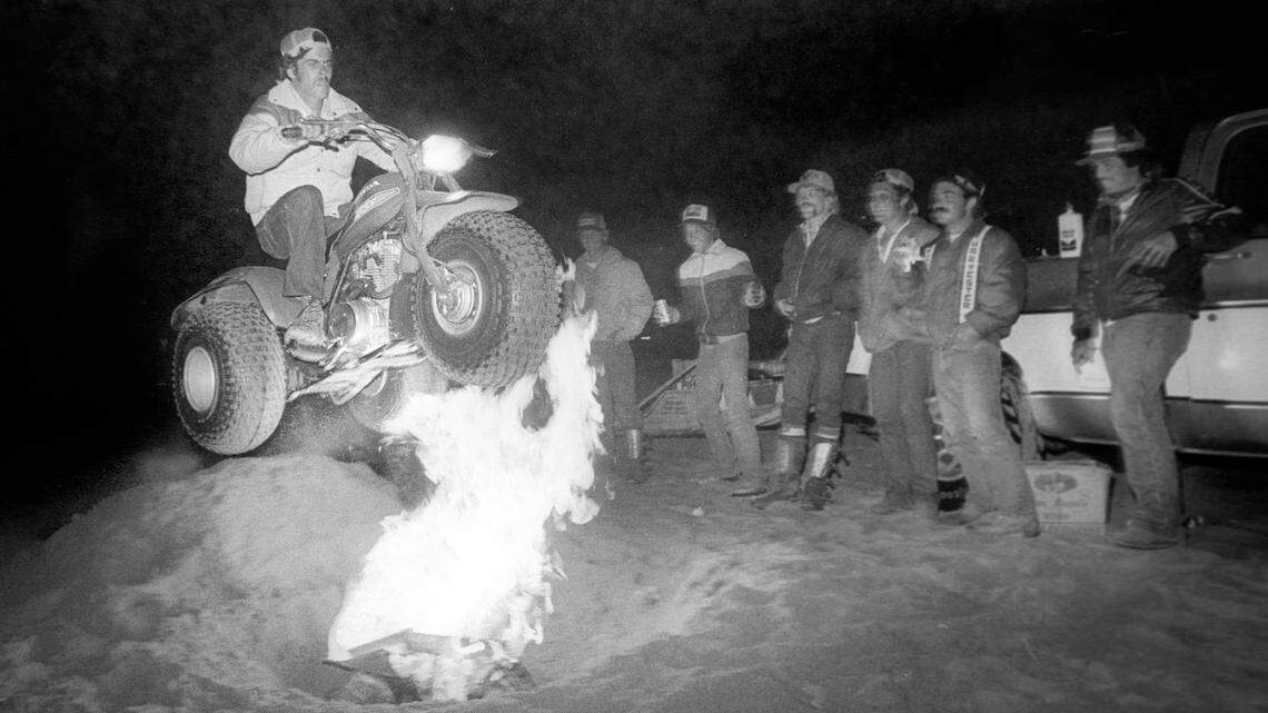 Joe Souza of Visalia soars across an open pit fire on his sand cycle as his buddies watch. They were among thousands of off-road enthusiasts who flocked to the Oceano Dunes for Labor Day Sept. 5, 1982.