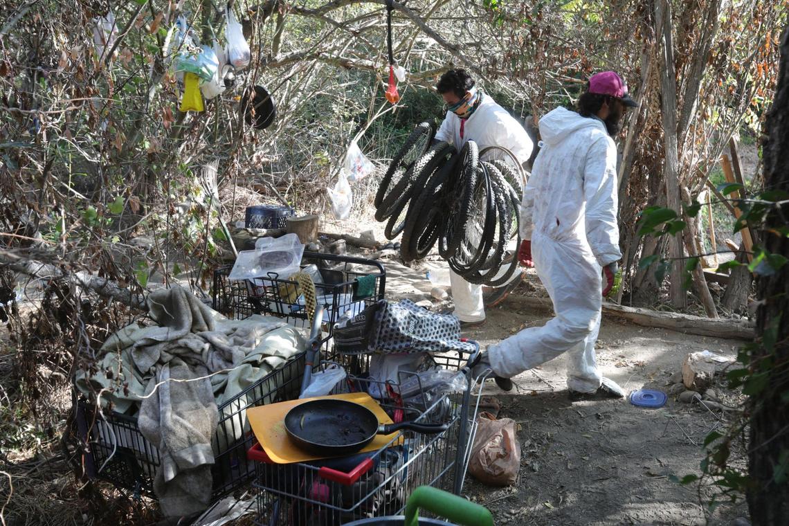 Jonathan Macis carries out an armful of loose bicycle wheels as he and Hector Noyola clear out a creekside camp in October 2020 in San Luis Obispo. They work for “2 Mexicans,” a hauling and project business. The city cleared out 58 homeless camps along the Bob Jones Trail from Prado Road to Los Osos Valley Road, in advance of winter weather.
