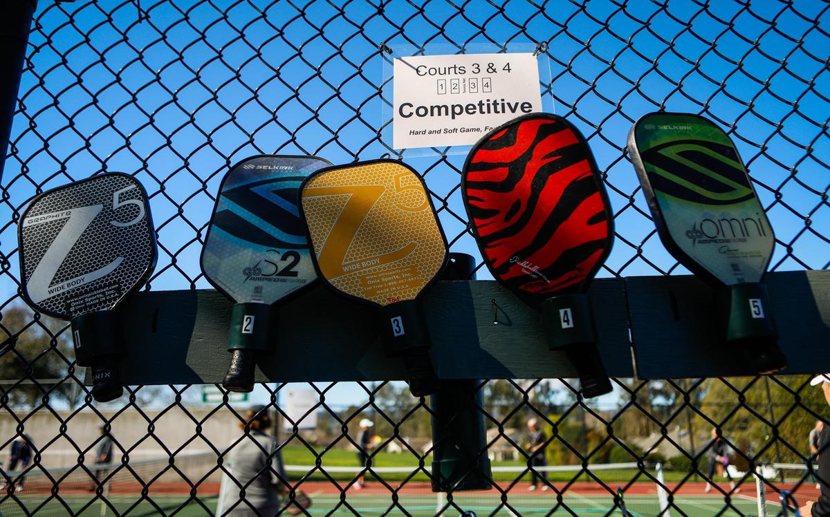 Pickleballers paddles hang on a fence by those awaiting an open court at French Park in San Luis Obispo, where three new courts will be going in. They will be first permanent pickleball courts in the city where there is a high demand to play.