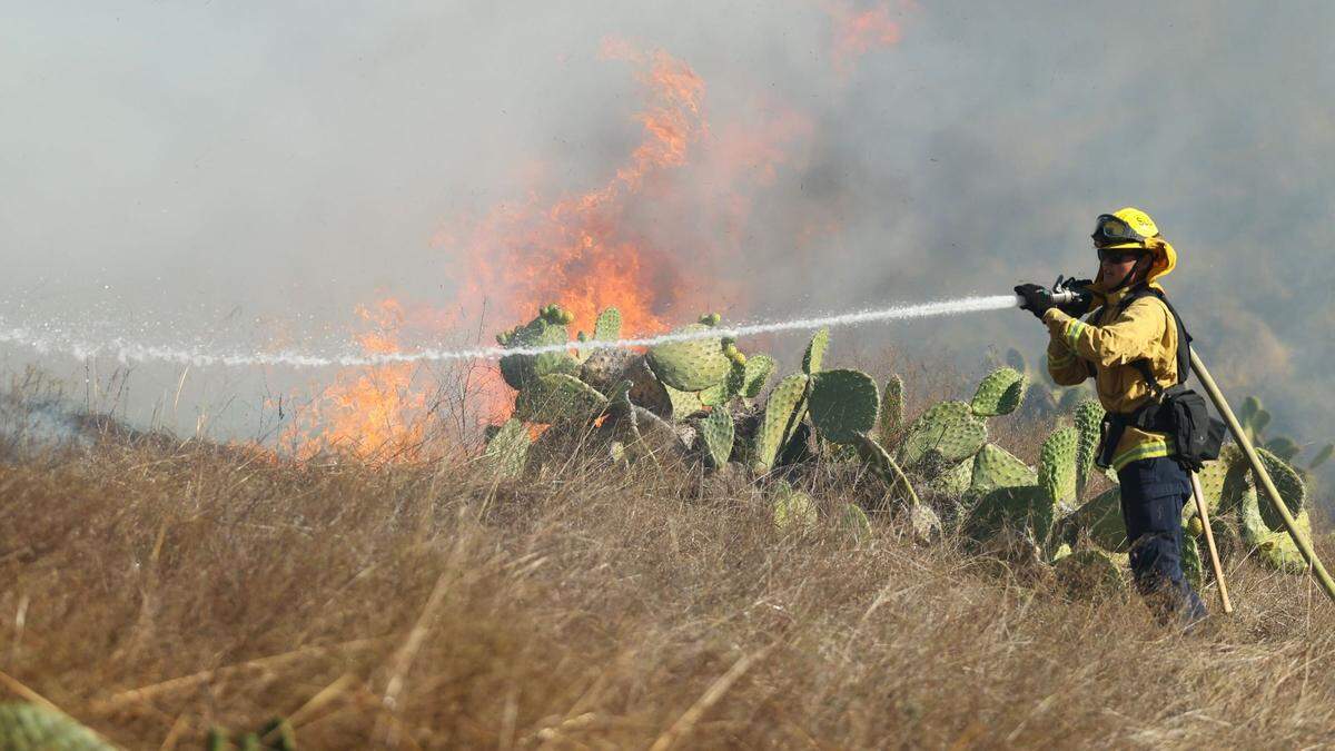 A firefighter works on to extinguish flames from a vegetation fire off Lizzie street in San Luis Obispo on Oct. 30, 2023. The fire apparently started behind the FFA farm at San Luis Obispo High School. Residents nearby were ordered to evacuate.