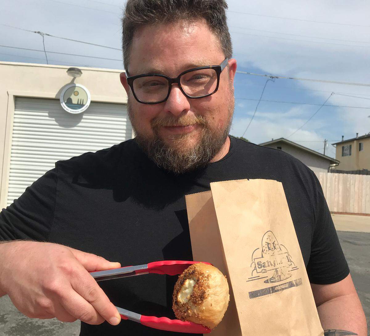 Salty Bagel owner Michael Milch bags up an order of his gluten-free bagels for a customer during a Friday afternoon pop-up at Avocado Shack in Morro Bay.