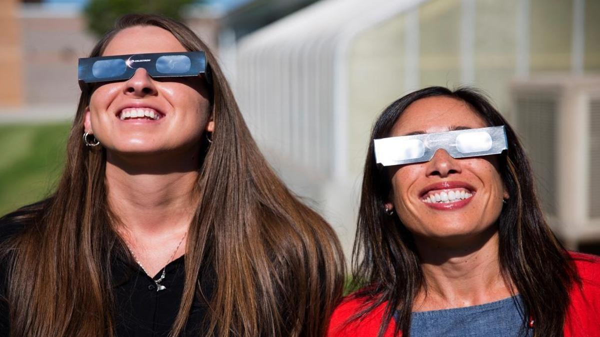 In this Tuesday, July 18, 2017 photo, Twin Falls High School science teachers Ashley Moretti, left, and Candace Wright, right, use their eclipse glasses to look at the sun as they pose for a portrait in Twin Falls, Idaho. Solar eclipse glasses are recommended to watch Monday’s eclipse.