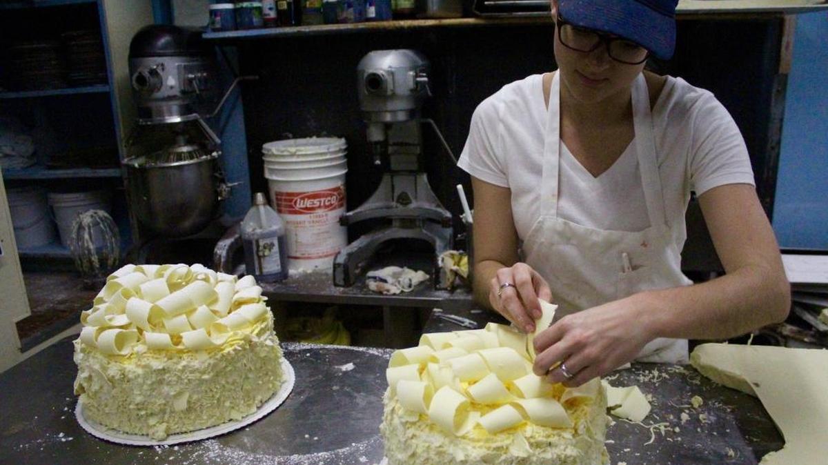 Kayla Klingenberg, a cake decorator at the Madonna Inn in San Luis Obispo, arranges white chocolate shavings on a pink champagne cake. The dessert is no longer pink due to FDA regulations on red food dye.