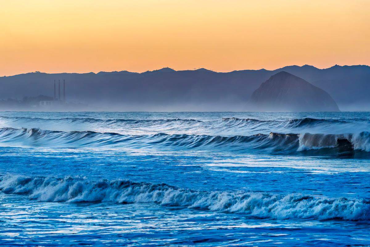 Waves crash in the Estero Bay with Morro Rock and the power plant stacks in the background.