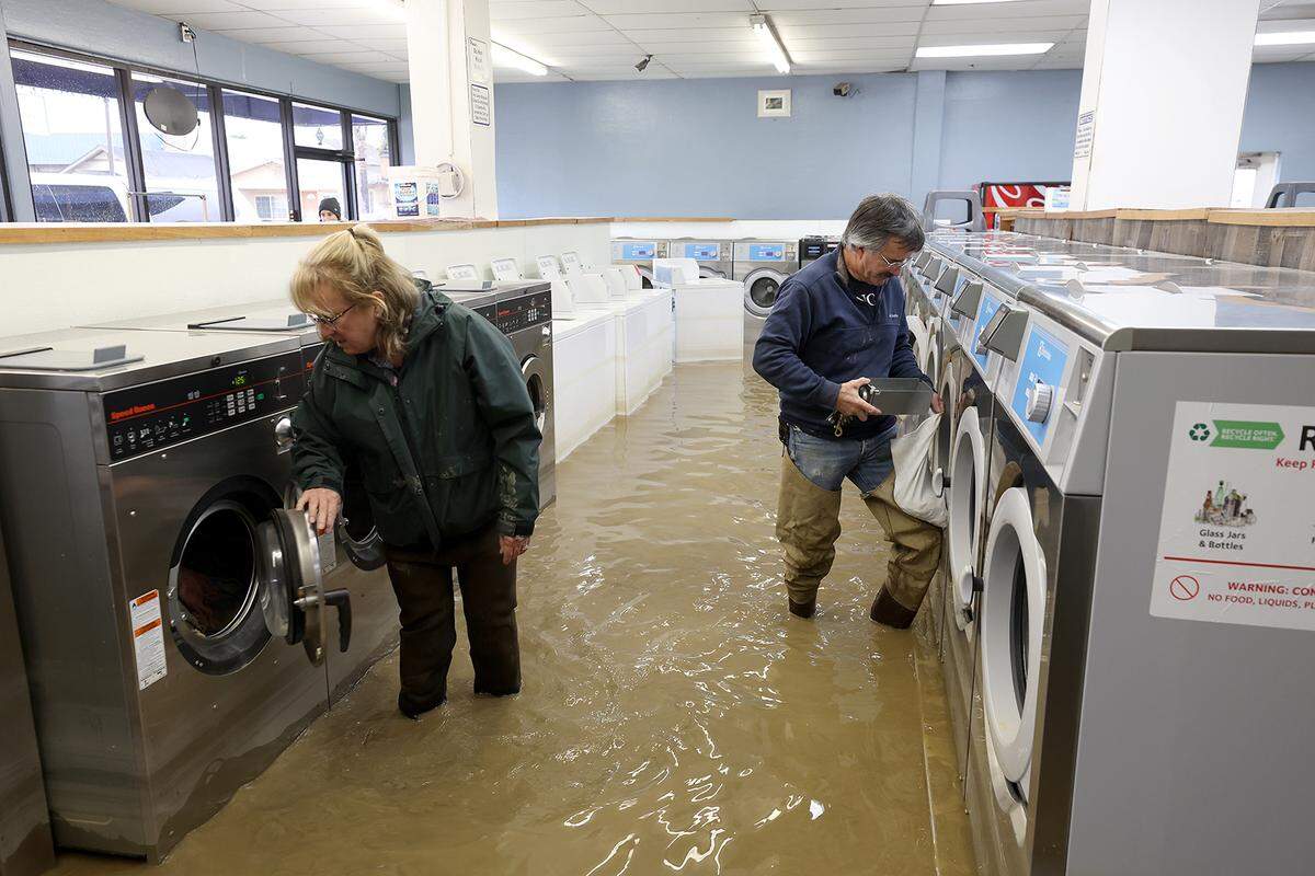 Patrick Cerruti (right) and his wife Pamela Cerruti take coins out of washing machines inside the flooded Pajaro Coin Laundry on March 14, 2023, in Pajaro, California. Northern California has been hit by another atmospheric river that has brought heavy rains and flooding throughout the region. The town has been inundated with floodwaters since Saturday after a levee was breached along the Pajaro River.