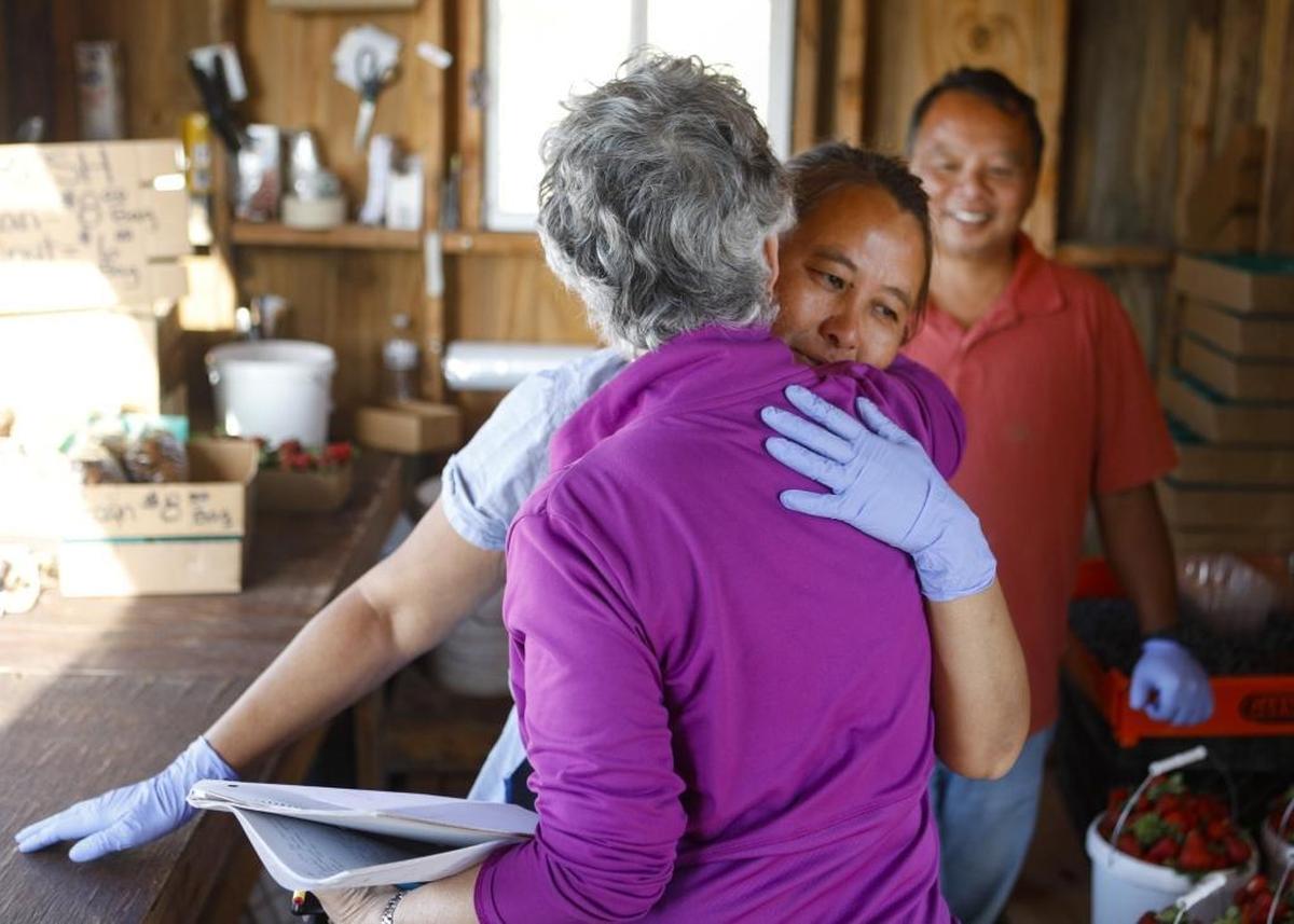 Nancy Peck hugs Meui Saelee as Saelee’s husband, Chan ChaoPharn, smiles in the background on Tuesday. Peck started a petition to persuade the county to allow Saelee and ChaoPharn to continue to operate their farm stand.