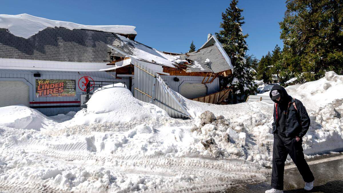 A man walks past a damaged tire shop in Crestline, Calif., Friday, March 3, 2023, following a huge snowfall that buried homes and businesses.