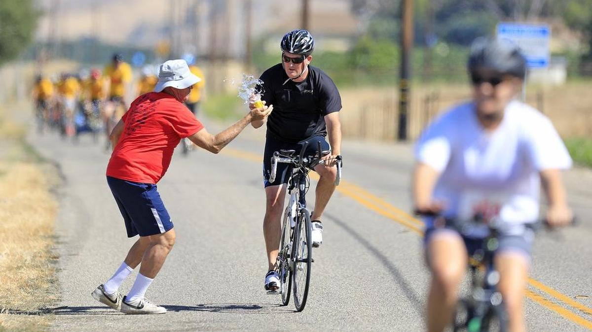 A bicycle rider grabs a cup from the water station volunteer during the 38th annual SLO Triathlon in 2017.