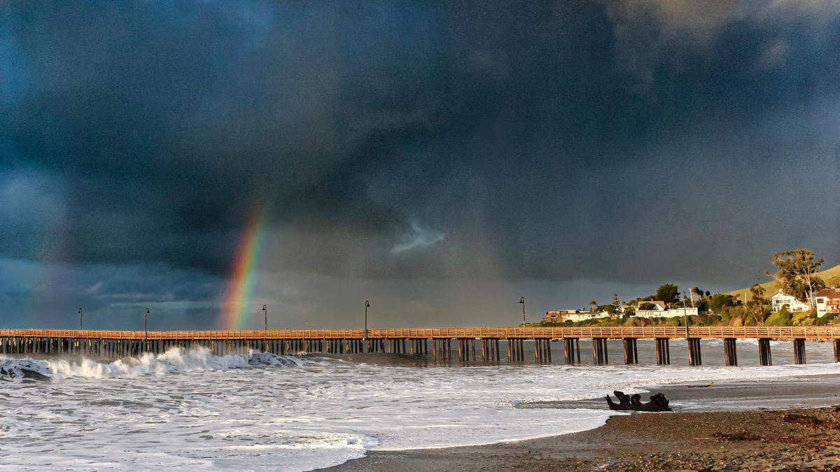 A rainbow breaks through storm clouds over Cayucos just after sunrise on Wednesday, Feb. 7, 2024. The pier was closed after sustaining damage from the weekend storms.