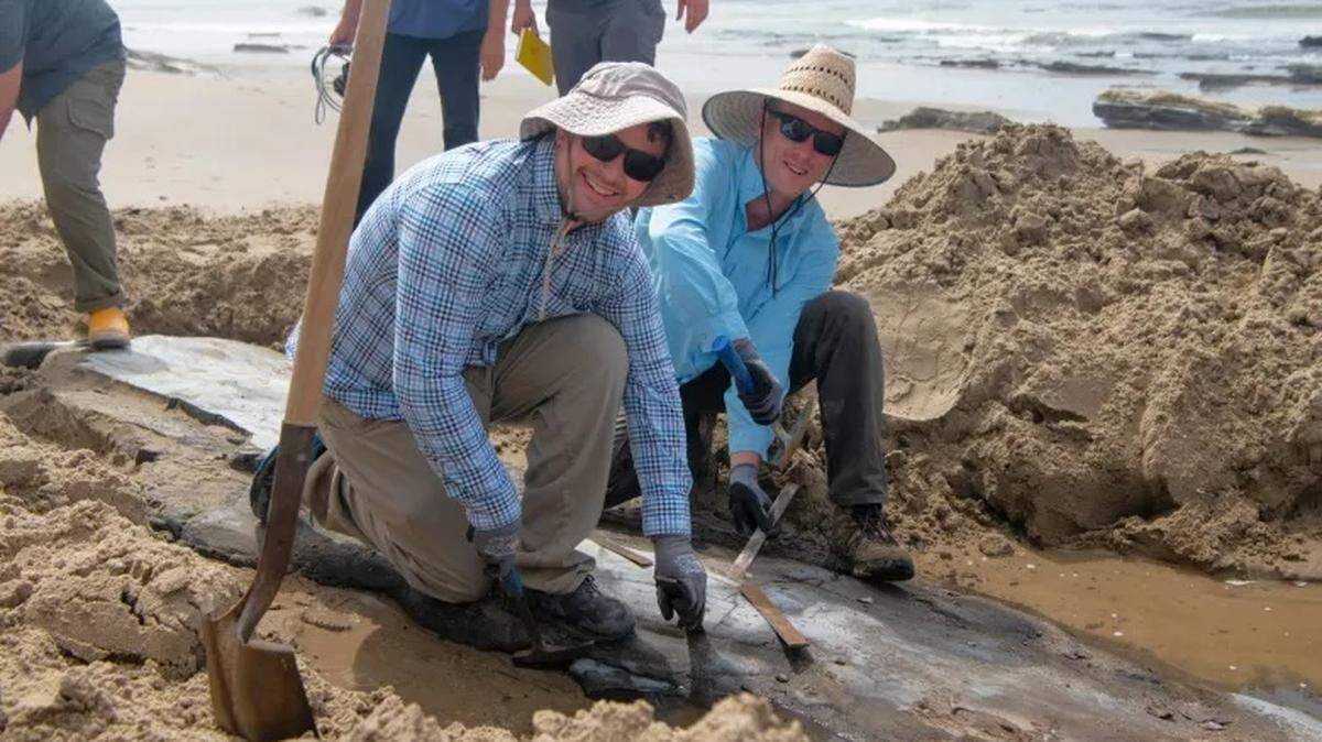 Chris Driesbach, left, and a volunteer stand over a whale fossil found along the Gaviota Coast. Driesbach, a geologist and fossil enthusiast, found the piece after the 2024 storm washed away sand from the surface.