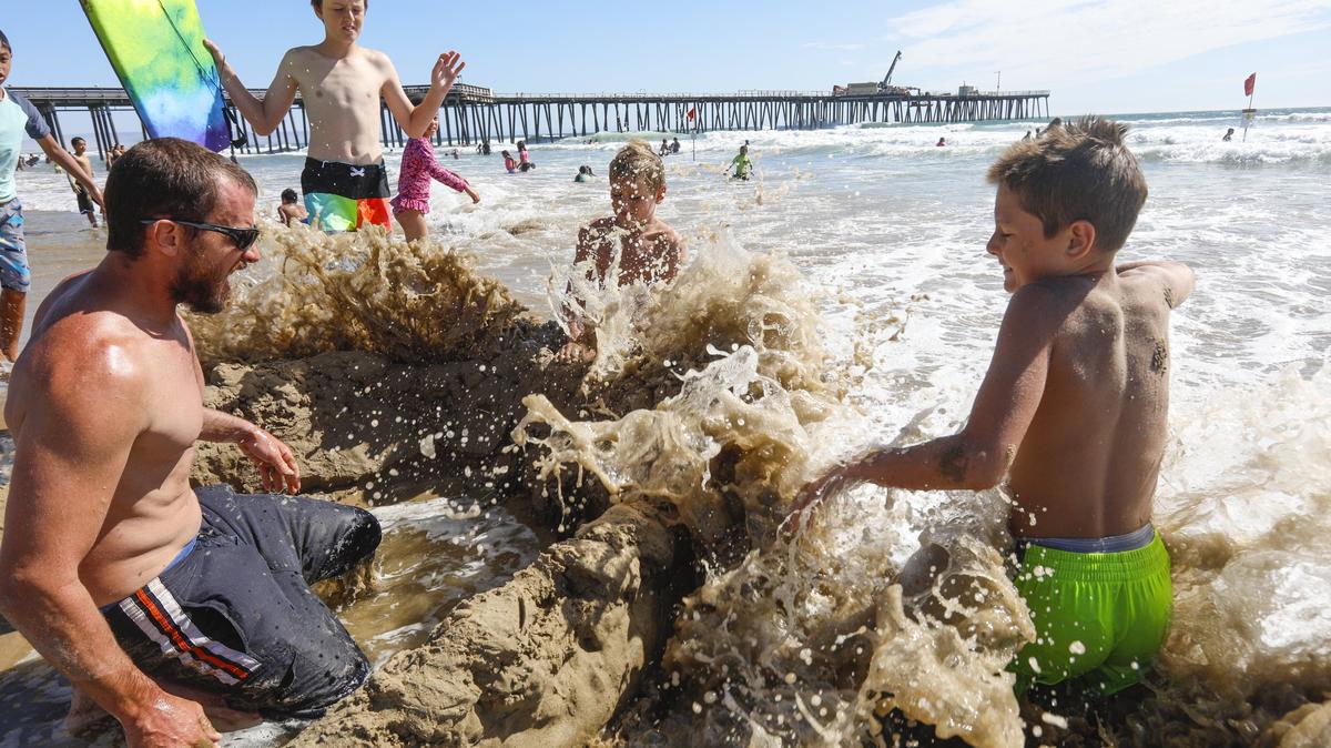 Conor Sullivan  and his sons, from left, Cohen, 14; Caen, 10, and Calen, 12, of Clovis work against the tide Friday to save their sand fortress. Crowds flocked to Pismo Beach as hot weather swept the region.