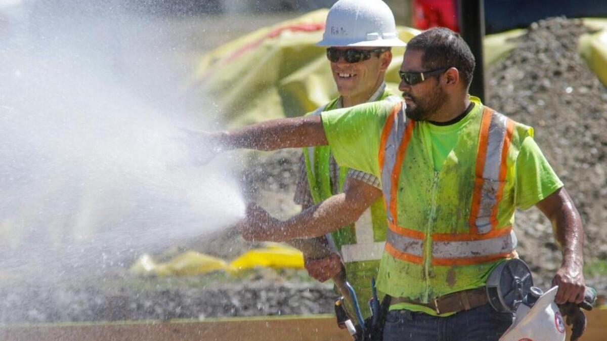 Working in triple-digit heat, David Ruble sprays a stream of water for Jacob Diaz to wet a cloth down to put under his helmet to keep cool Tuesday in San Luis Obispo. Workers at the new San Luis Obispo High School tennis courts were setting out reinforcing bar spraying water down to compact sand in advance of pouring concrete.