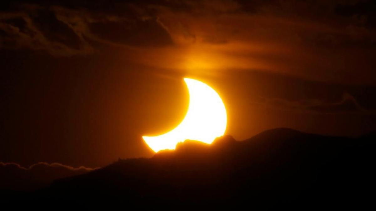In this May 20, 2012, photo, the annular solar eclipse is seen as the sun sets behind the Rocky Mountains from downtown Denver. A total solar eclipsewill cut a diagonal path across the U.S. next month.