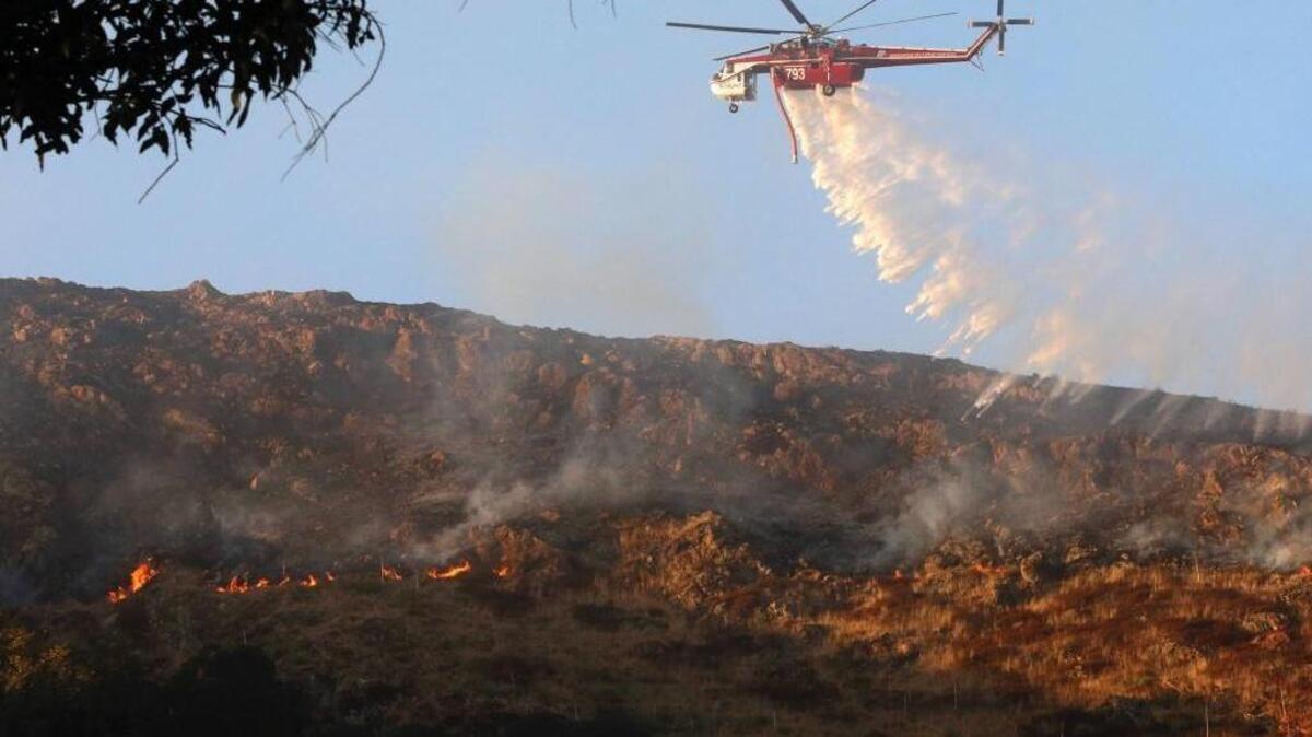 A helicopter makes a drop on a line of flames burning above homes near Cuesta Park in San Luis Obispo on September 27, 2017.