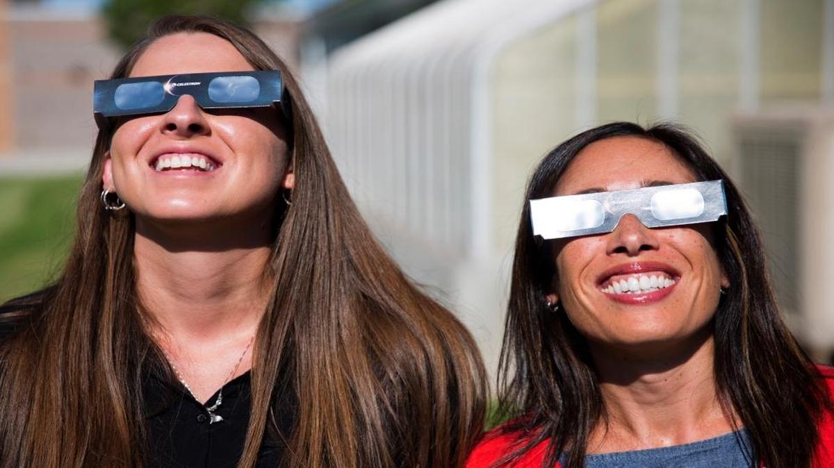 Twin Falls High School (Idaho) science teachers Ashley Moretti, left, and Candace Wright, right, use their eclipse shades to look at the sun as they pose for a portrait. The district bought 11,000 pairs of solar glasses, enough for every student and staff member to view the solar eclipse Aug. 21, from Twin Falls.