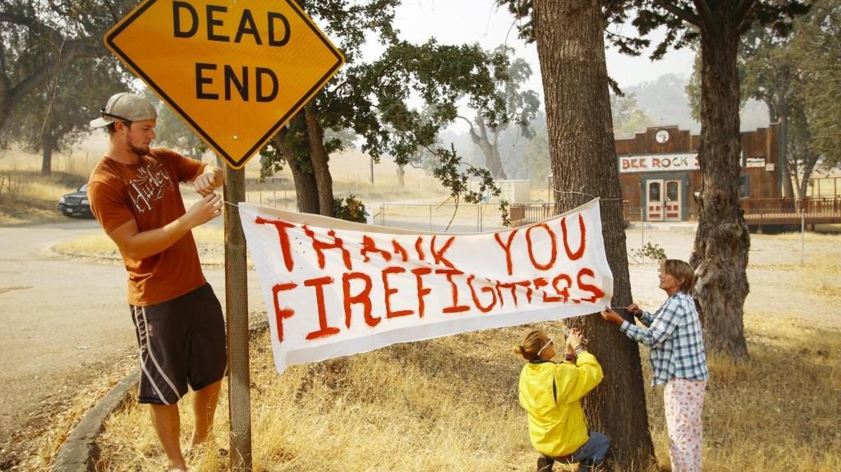 Dawn Leigh Doiel, right, her daughter Mallory Doiel-Glisson, and her nephew Nate Broden hang a banner thanking firefighters battling the Chimney Fire at the intersection of Interlake and Bee Rock Roads in Paso Roblesin August.
