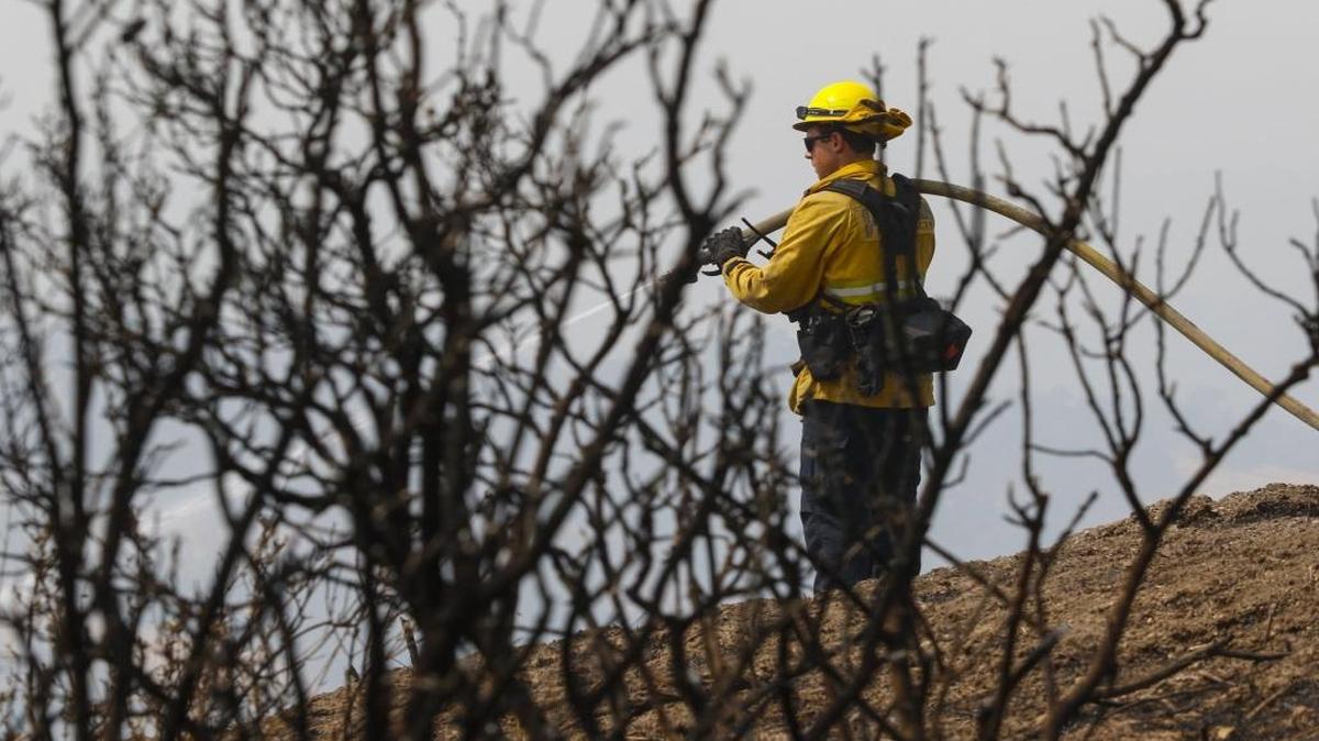 Kit Hentzen stands amid burnt brush as he sprays foam on hot spots near Oak Shores.