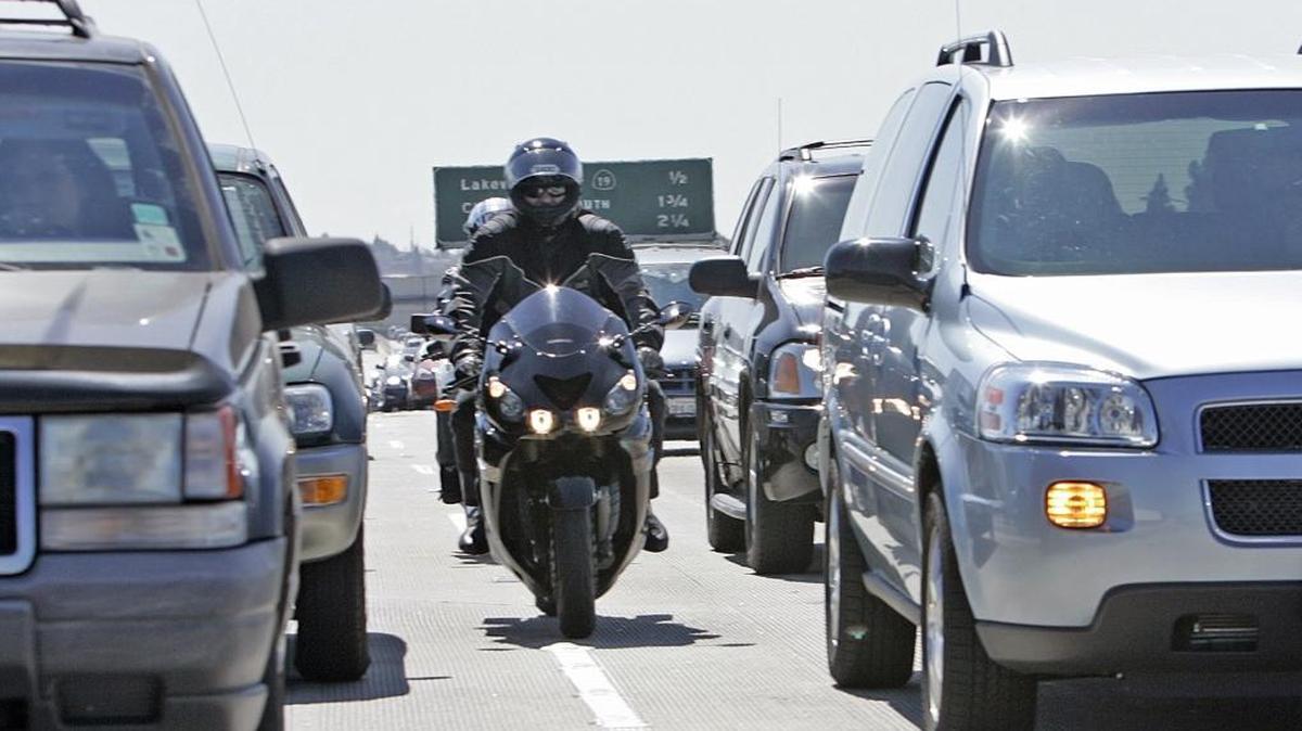 A motorcycle drives between cars on the highway.