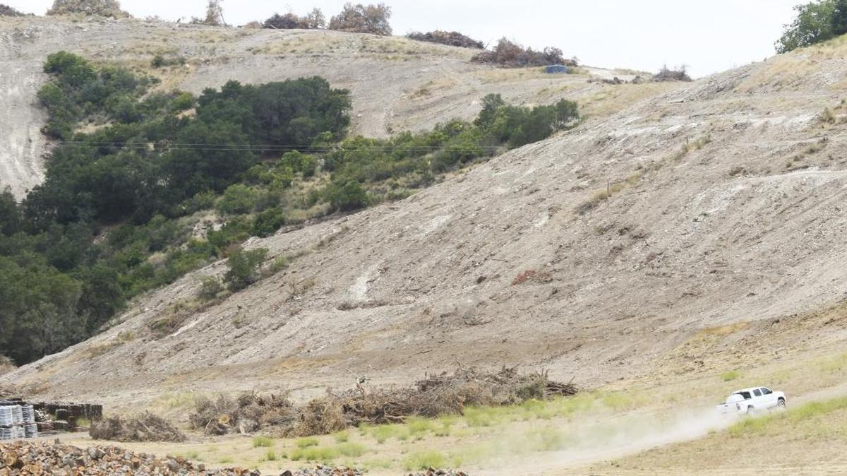 A pickup truck drives through piles of oak wood and scraped hillsides in a canyon off of Willow Creek Road.