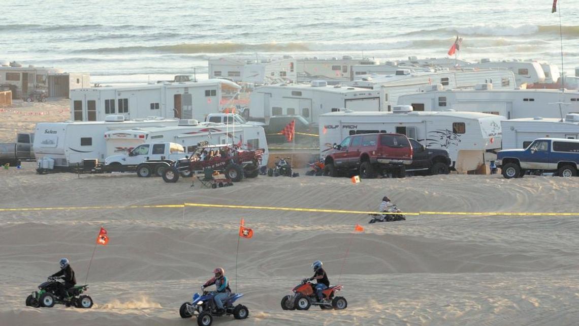 Camping trailers bunch together on the beach at the Oceano Dunes while riders on quads cruise through the sand nearby.